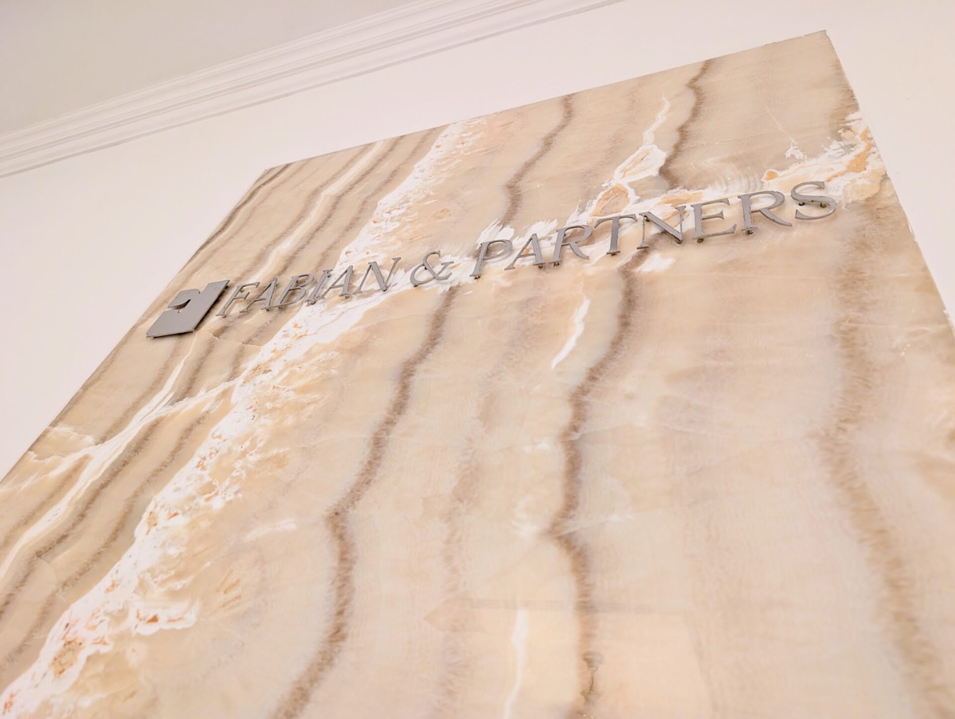Marble wall sign with metallic letters reading 'FABIAN & PARTNERS' on a beige surface