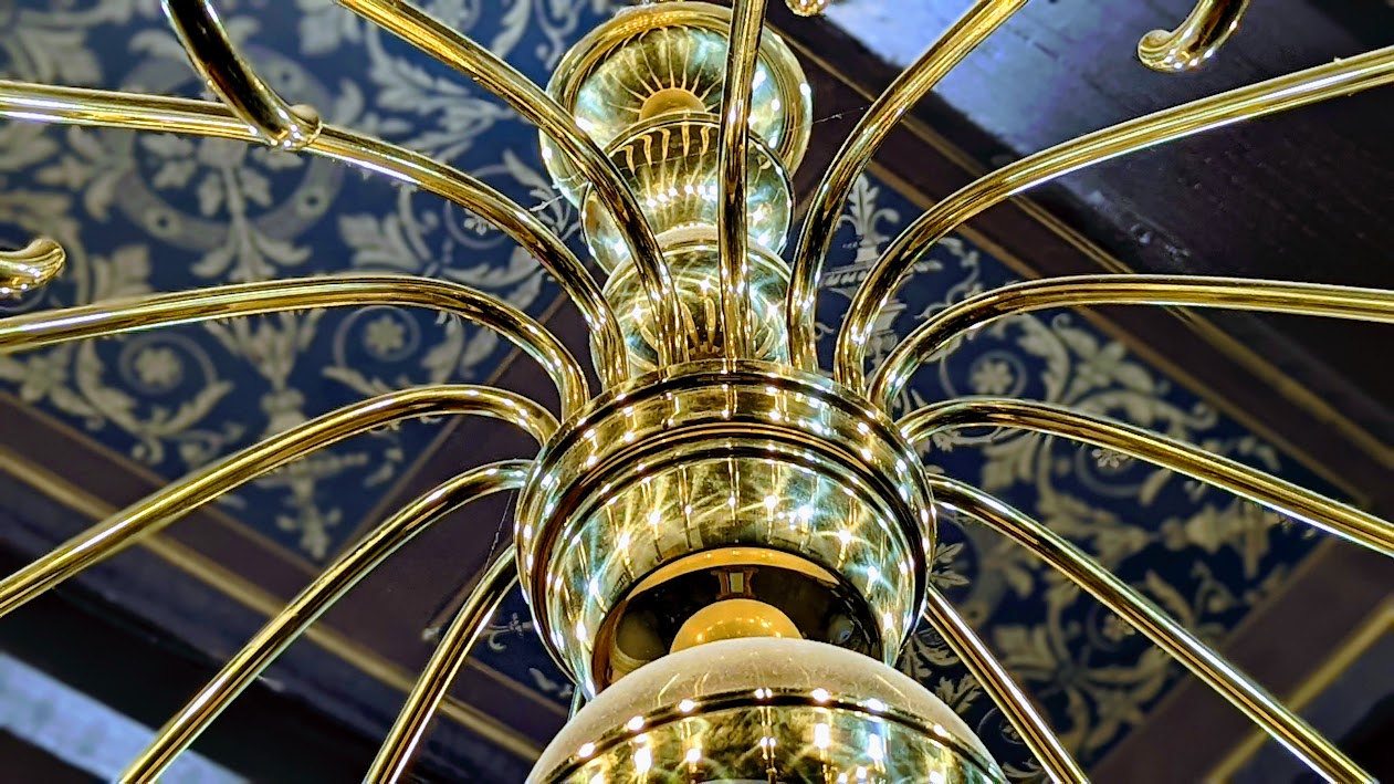 Vymáhání-dluhopisy-wood-seeds-insolvence Close-up of a gold chandelier centerpiece with curved arms and glowing bulbs surrounding a central column.